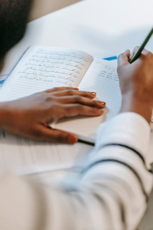 Unrecognizable ethnic woman writing information in notepad