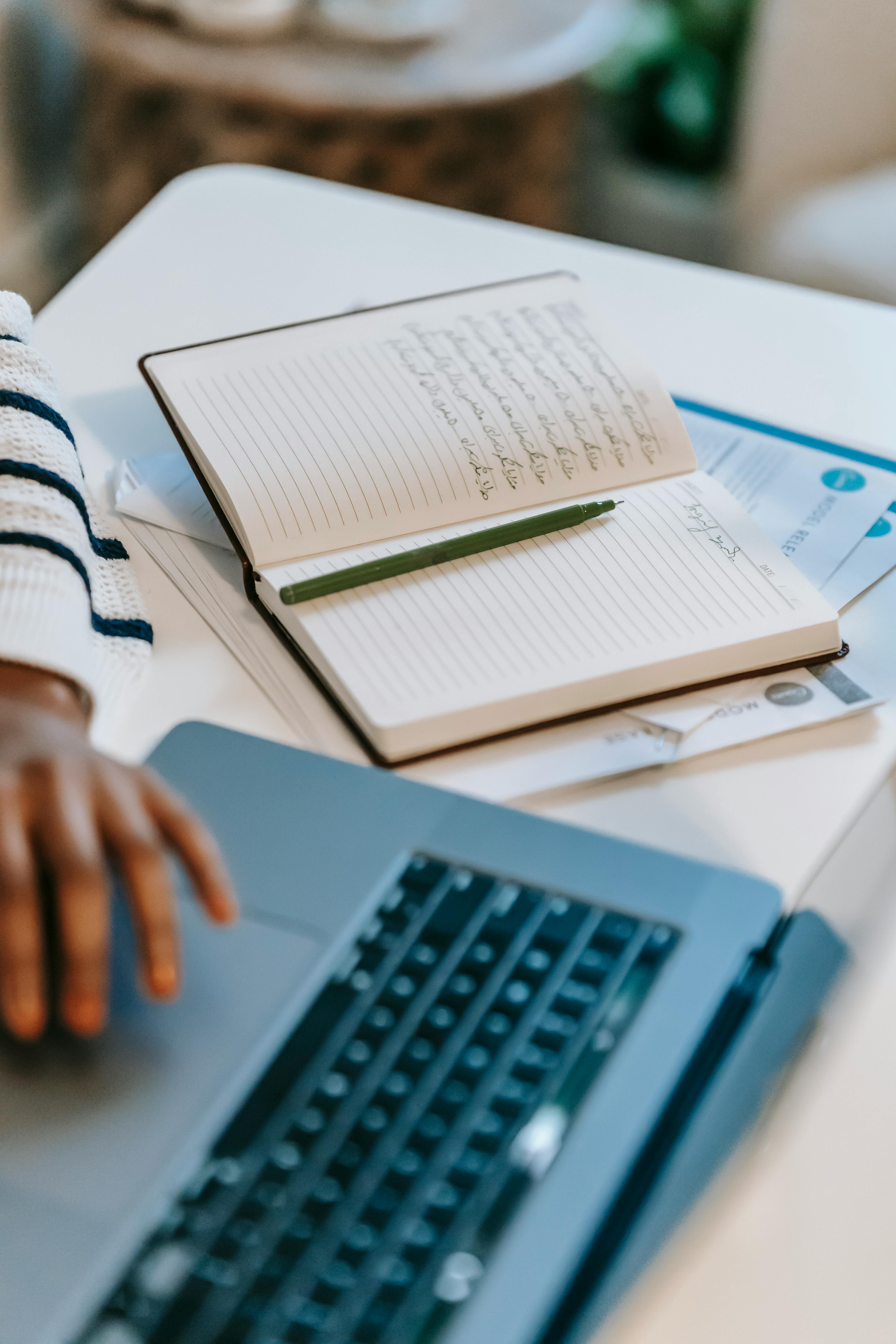 unrecognizable ethnic female freelancer using laptop near notepad