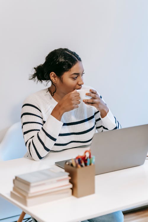 Ethnic female freelancer using laptop at table with coffee cup