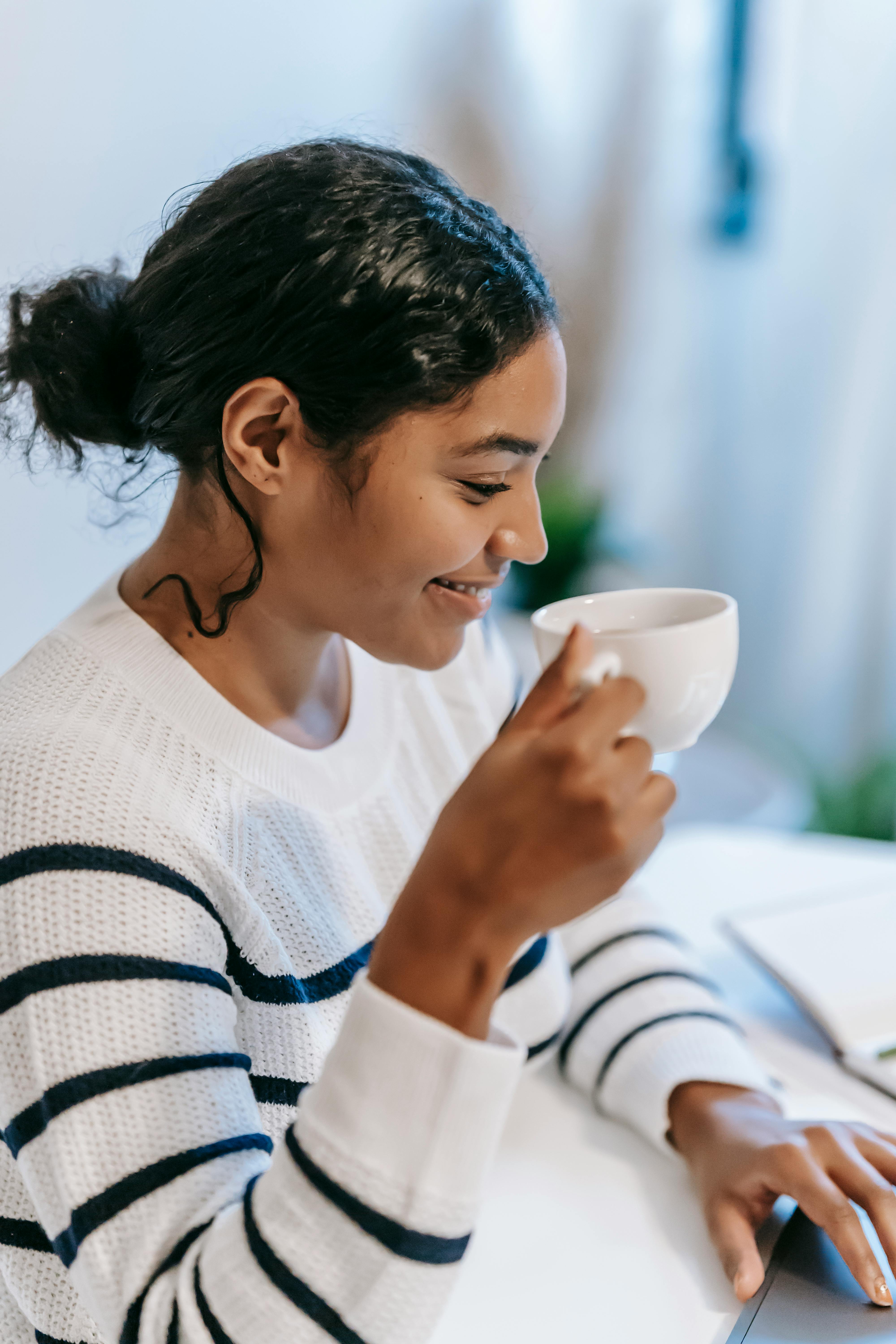 ethnic female freelancer using laptop and drinking coffee in workplace