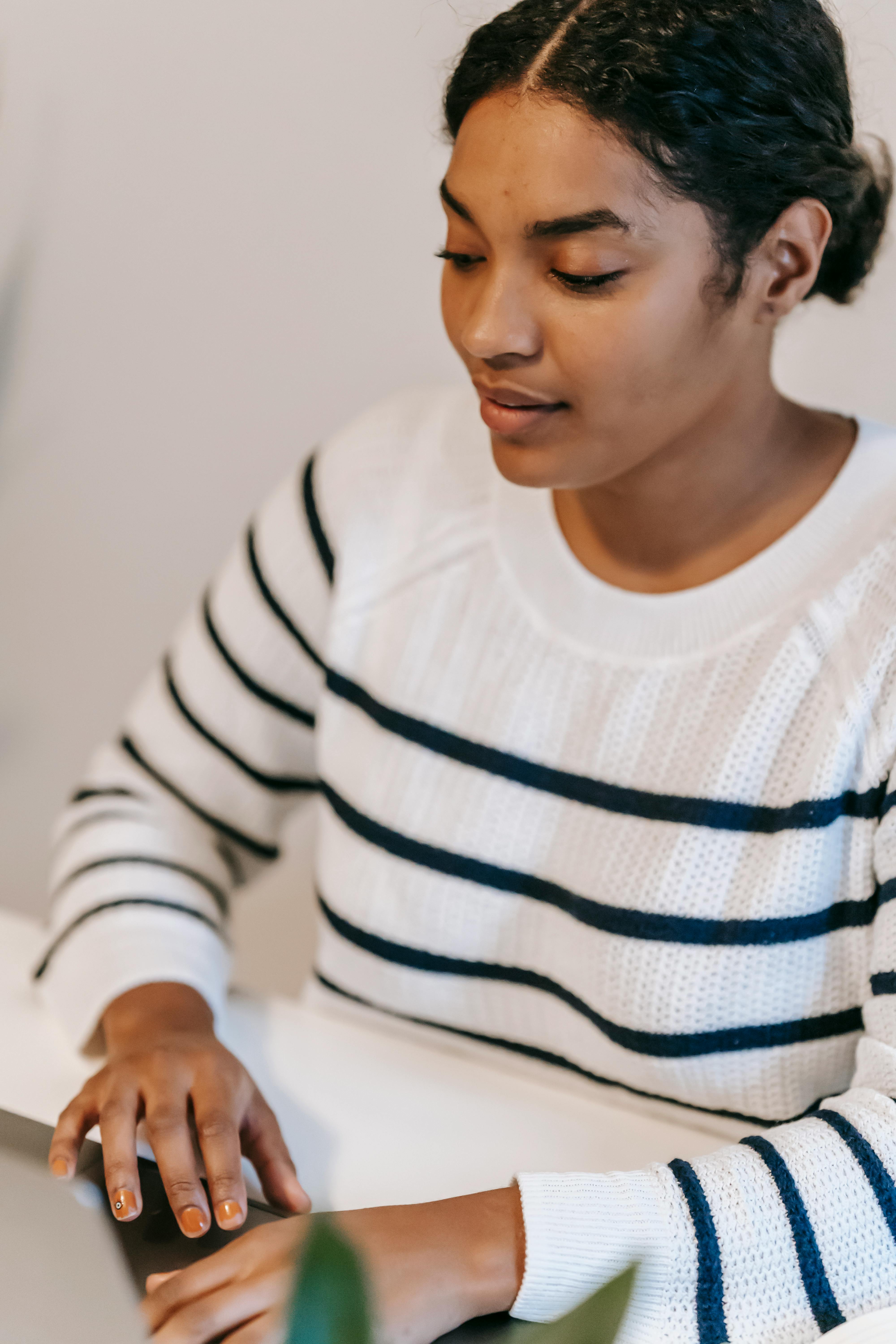 Confident Indian woman in casual clothes working remotely on laptop at table near green plant in light room