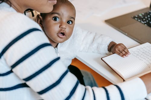 Indian child with woman in casual clothes at table with opened notepad and netbook in light flat