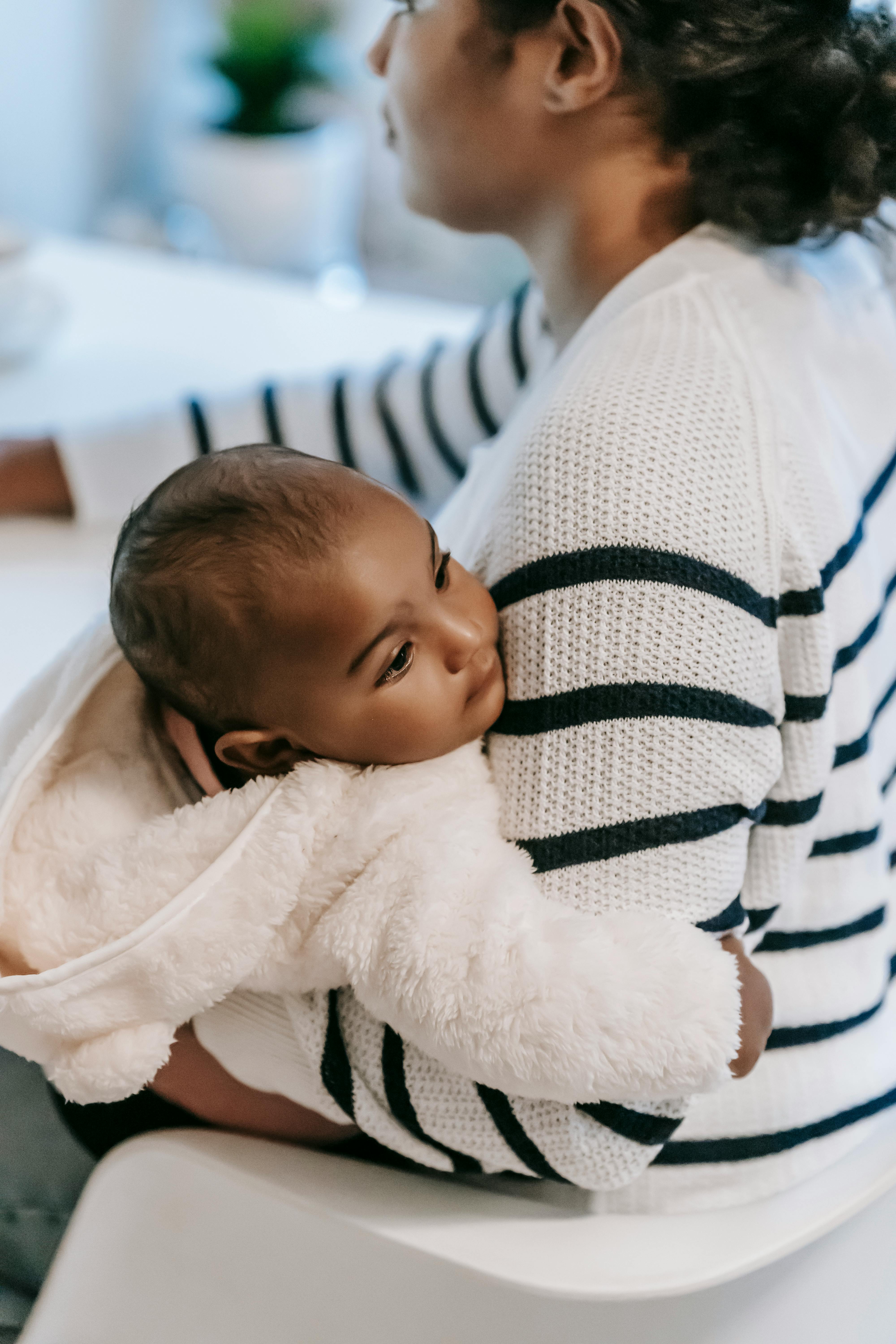 Ethnic mother with baby on laps near table in house