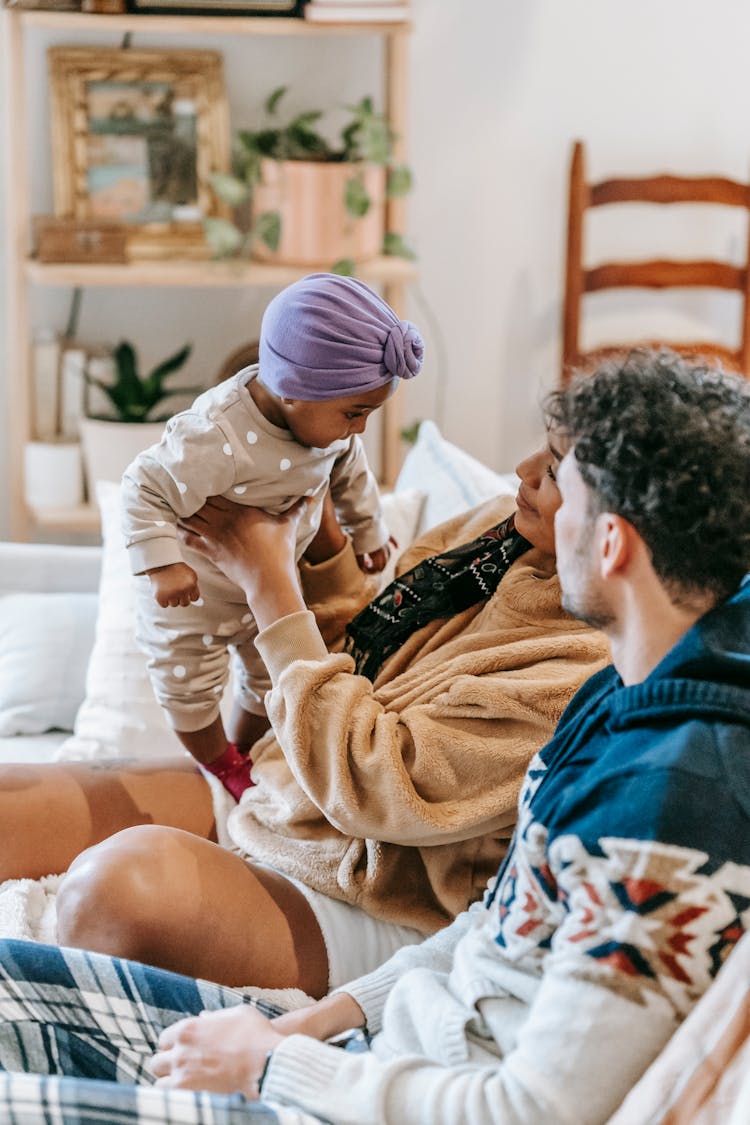 Couple With Baby Sitting On Sofa In Room