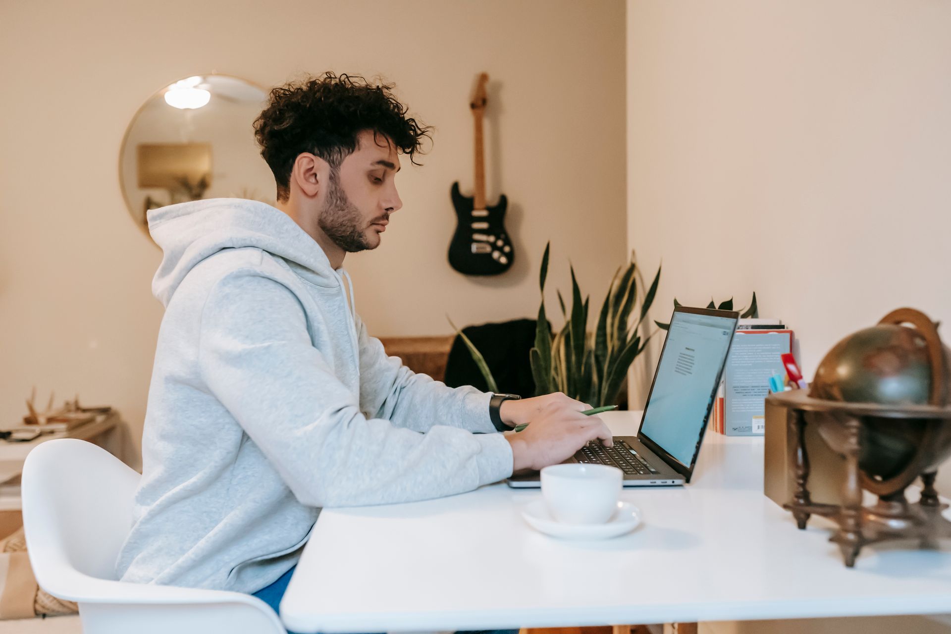 Side view of concentrated student with dark curly hair in casual clothes sitting at table and browsing netbook in room in daytime