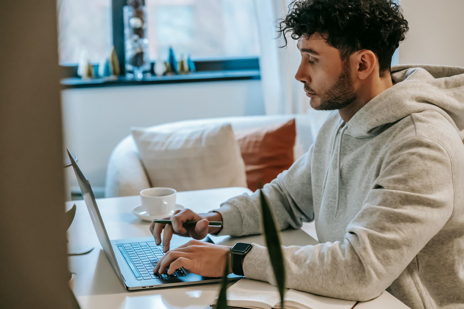 Side view of crop focused male remote worker browsing internet on netbook at table with coffee in house