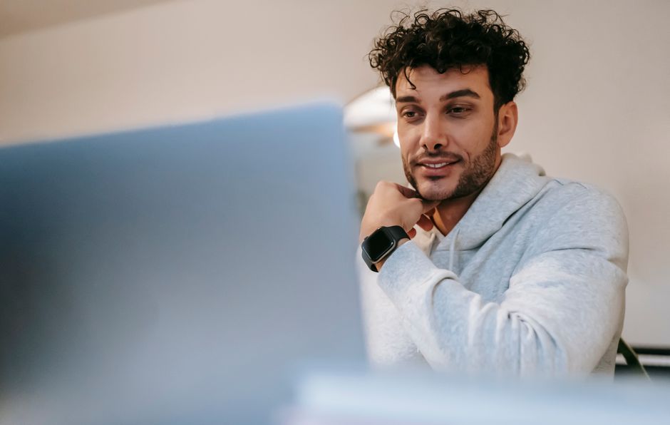 Young friendly unshaven male remote worker in wearable tracker against netbook in light house room