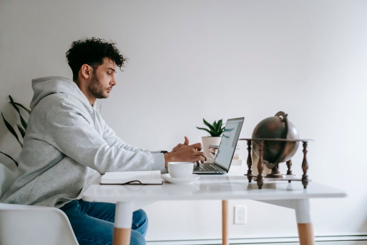 Pekerja remote duduk di rumah membuka laptop untuk mengerjakan proyek freelance side hustle tambahan