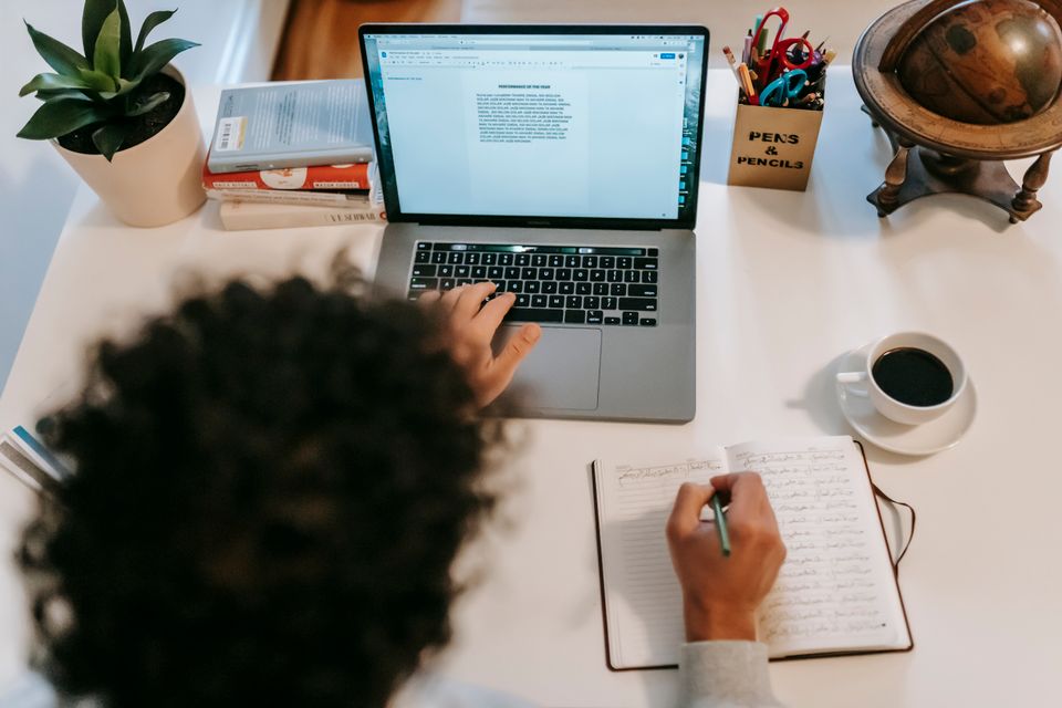 Writer drafting an article on a laptop with a notebook beside it