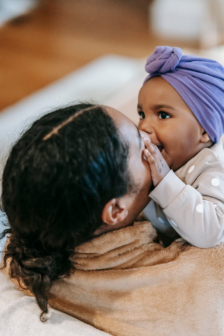 Cute Black Baby Biting Face Of Unrecognizable Mom At Home