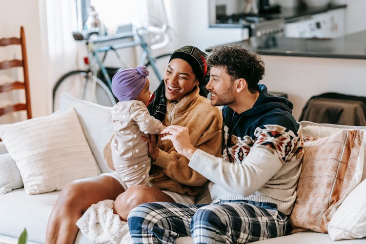 Happy Diverse Family Talking To Little Girl On Sofa Indoors