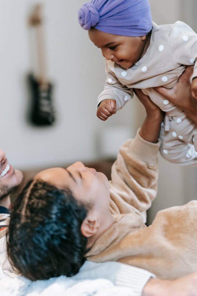 Black Mother Raising Happy Baby Near Crop Father At Home