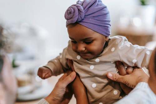 Free Crop anonymous multiethnic family interacting with cute little girl in headscarf while spending time in house Stock Photo