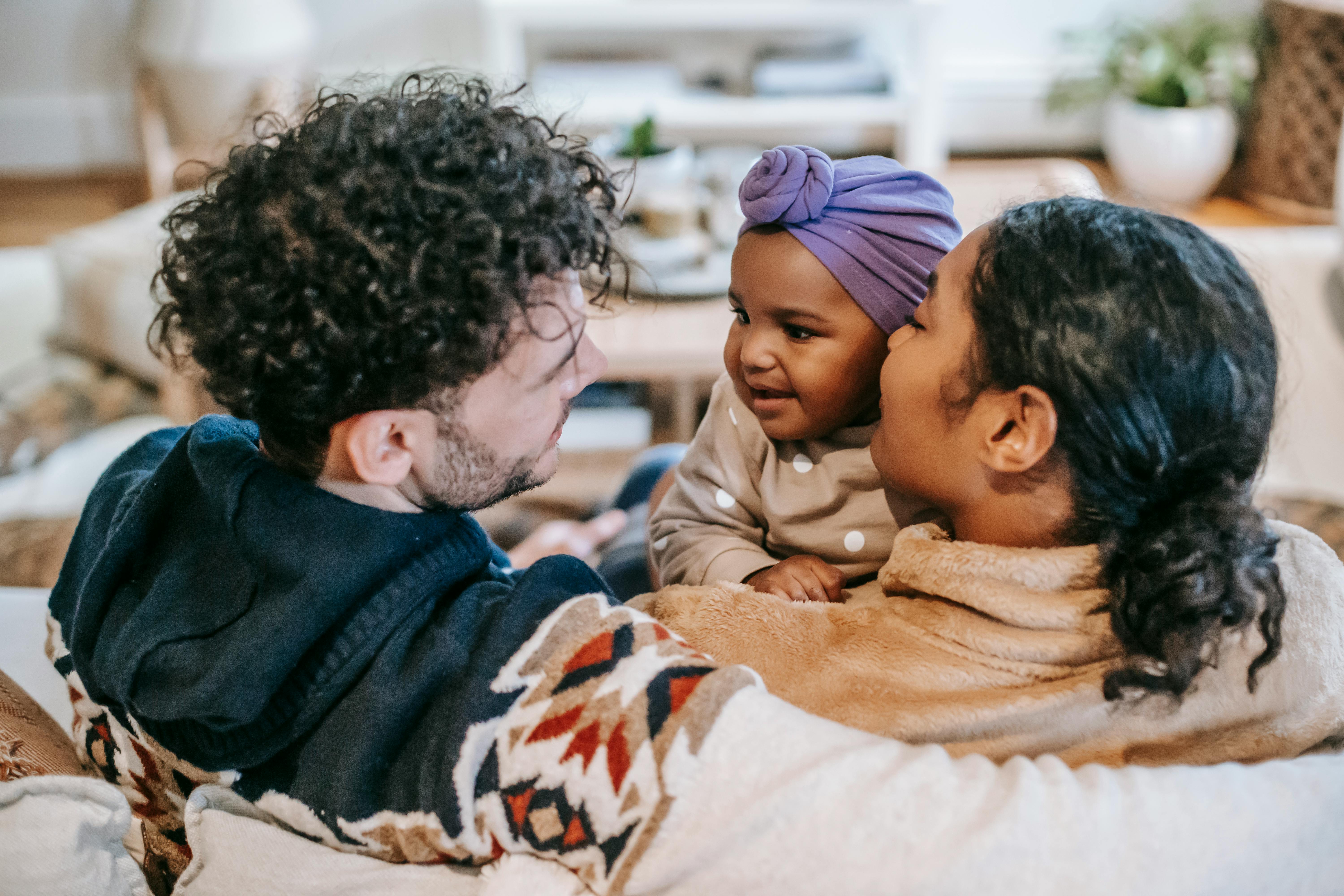 smiling multiracial family interacting with little girl in house