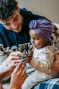 Crop smiling father and unrecognizable black mom demonstrating conical decoration to attentive little girl in house room