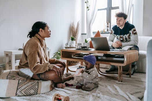 Full body of serious ethnic man sitting near computer in living room with black woman and little toddler at home