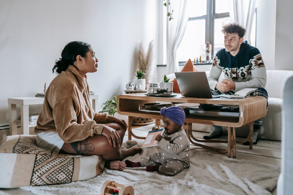 Free Full body of serious ethnic man sitting near computer in living room with black woman and little toddler at home Stock Photo