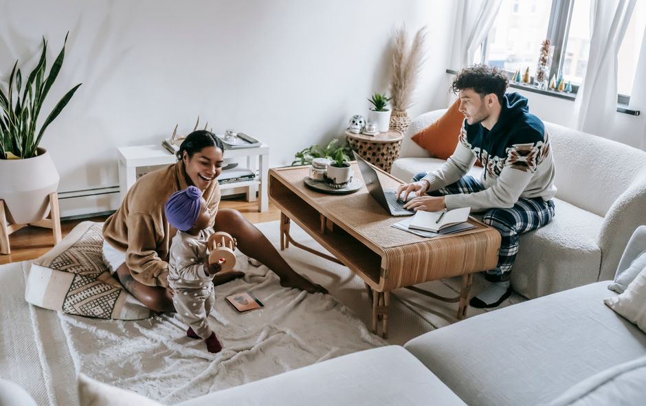 From above full body of ethnic man typing netbook while working in living room with cheerful African American mother and little toddler