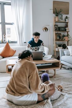 Faceless mother with little baby sitting on floor in living room with ethnic father typing on netbook while working at home
