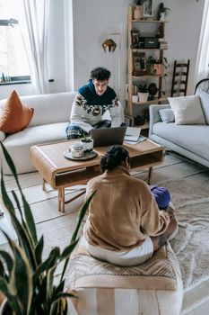 From above of anonymous mother and little toddler sitting in living room near ethnic father typing on netbook during remote work at home