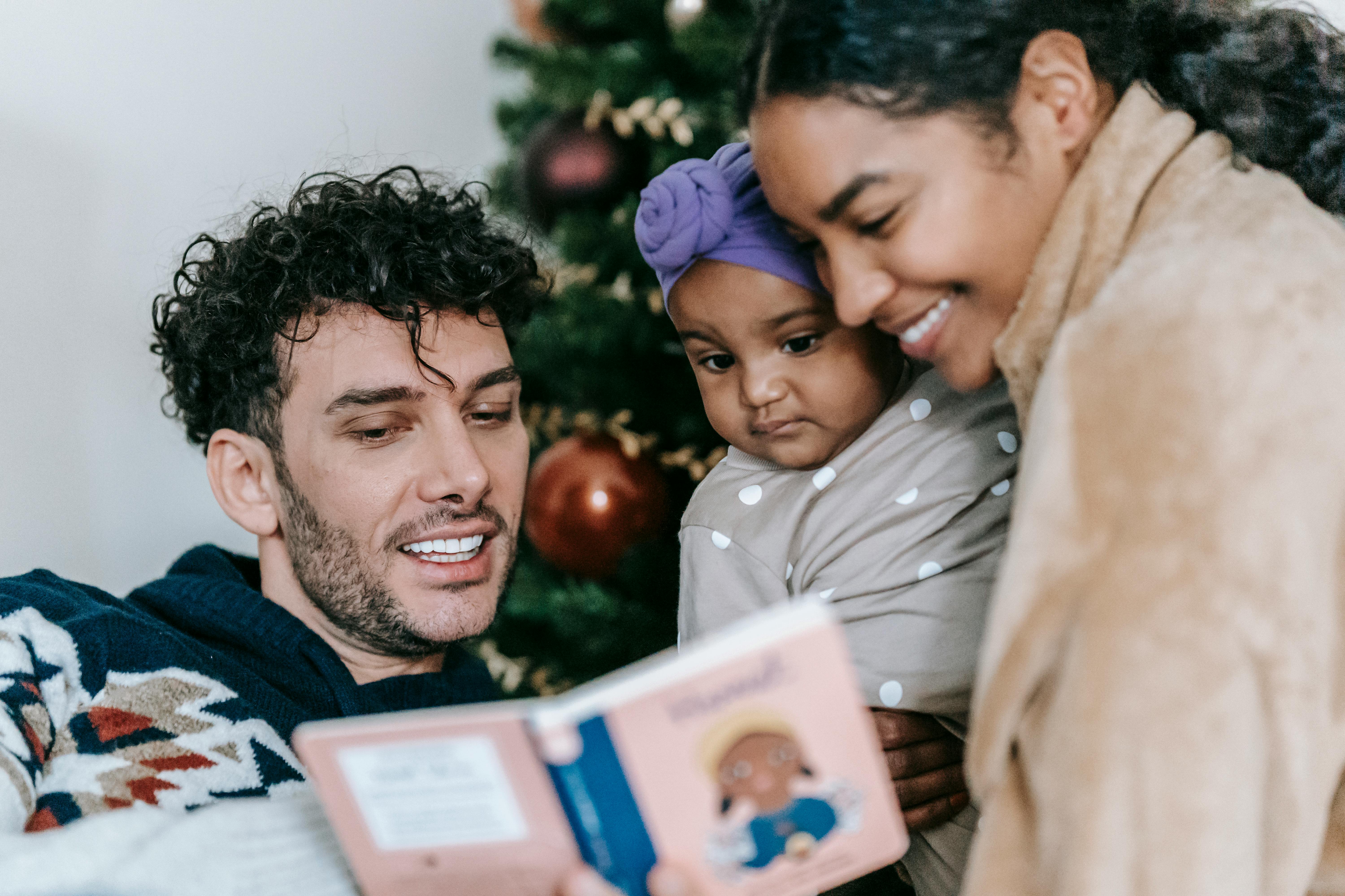 diverse parents reading book to baby near christmas tree