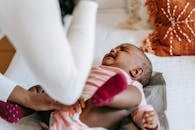 From above of crop anonymous mom soothing sweet small African American girl on bed