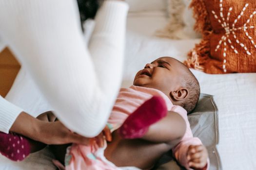 From above of crop anonymous mom soothing sweet small African American girl on bed