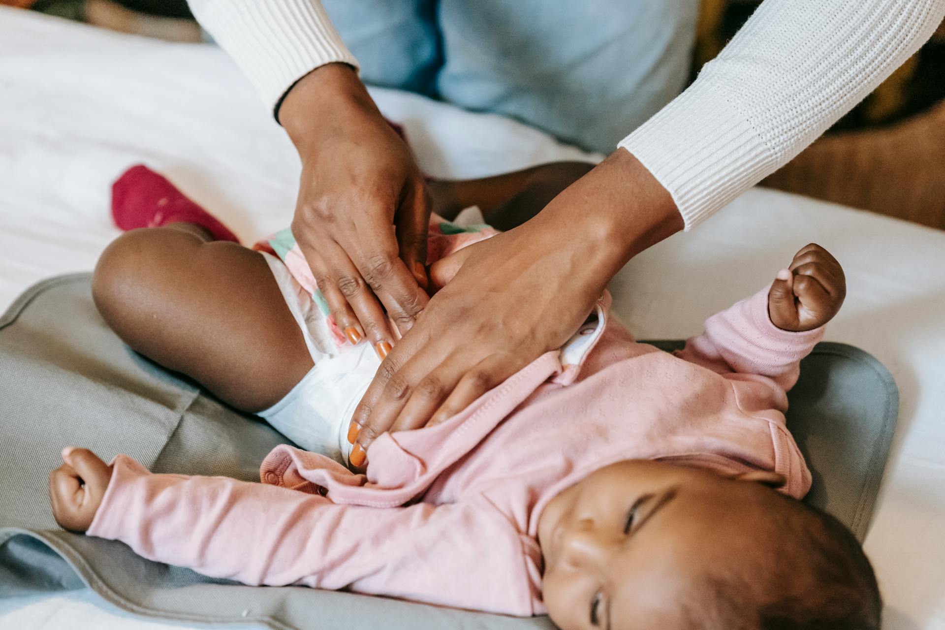 A caregiver gently changing a baby's diaper indoors, showcasing love and care.