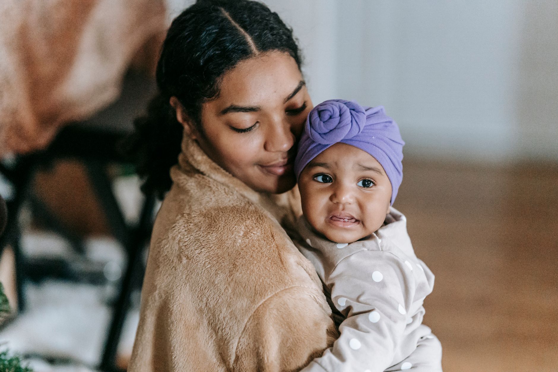 Crop ethnic mother with small African American displeased small adorable daughter on blurred background of apartment