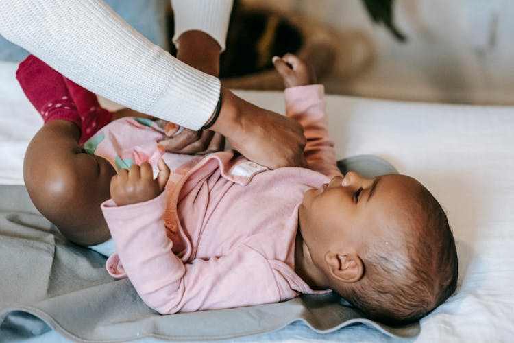 Black Mother Putting Clothes On Ethnic Baby Lying On Blanket