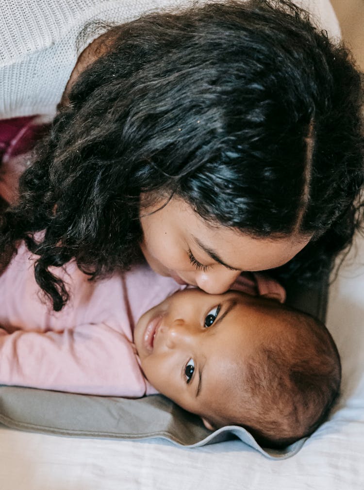 Black Mother Kissing Baby Lying On Blanket