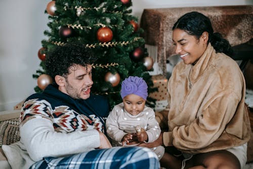 Happy parents having pleasant time with baby against Christmas tree