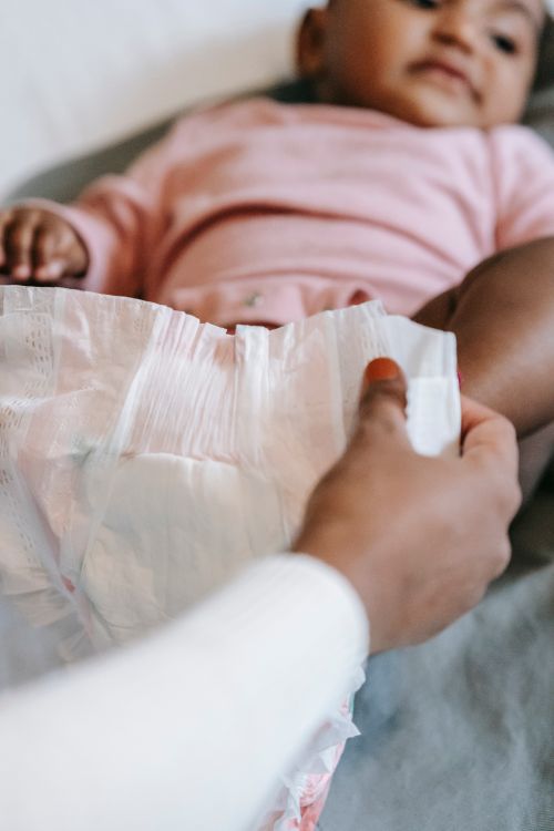 Free Crop anonymous ethnic mothers holding diaper while dressing calm baby lying on bed at home in daytime Stock Photo