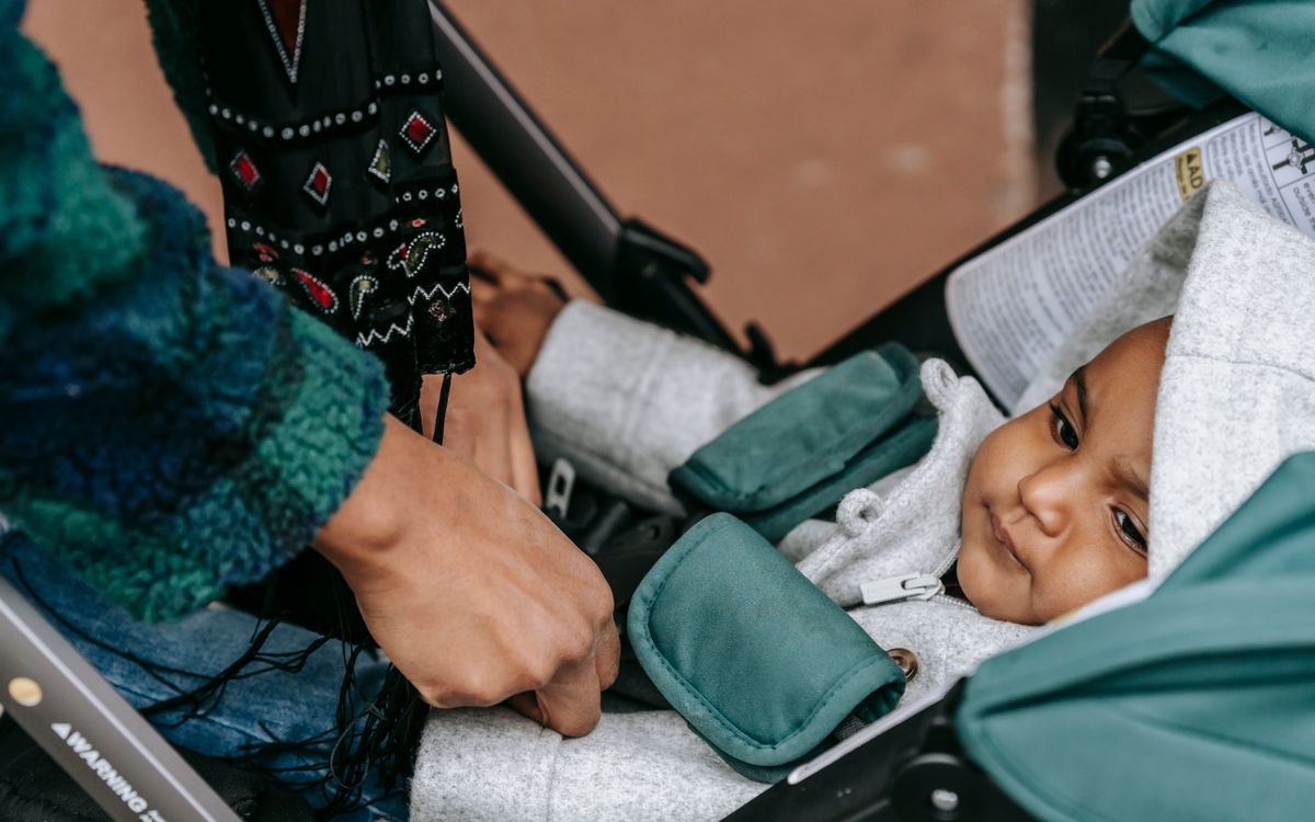 Crop anonymous ethnic mother adjusting clothes of baby lying in stroller and looking away on street in daytime