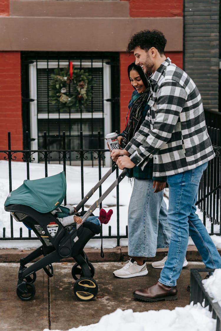 Ethnic Couple Walking With Stroller On Street In Winter Time