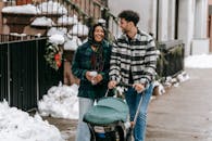 Happy ethnic couple walking with stroller on street in residential city district