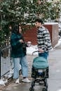 Side view of calm ethnic couple in casual clothes standing near metal fence and tree on street and communicating during walk with baby in stroller in daytime