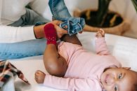 High angle of crop African American mother putting jeans on baby daughter crying on changing table
