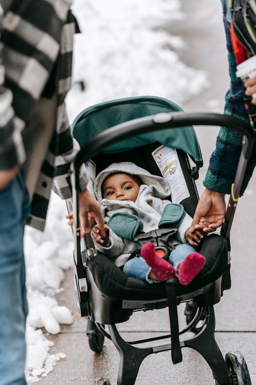 Free Ethnic baby lying in stroller during stroll with parents Stock Photo