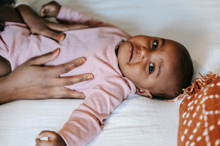 Black Mother Stroking Baby Lying On Bed