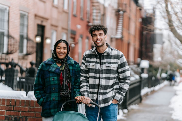 Young Ethnic Couple Standing With Stroller On Sidewalk