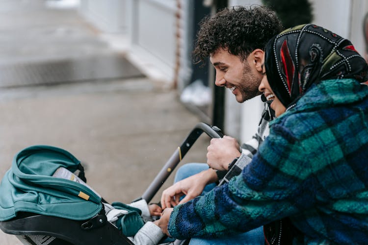 Ethnic Couple Smiling At Baby Lying In Stroller