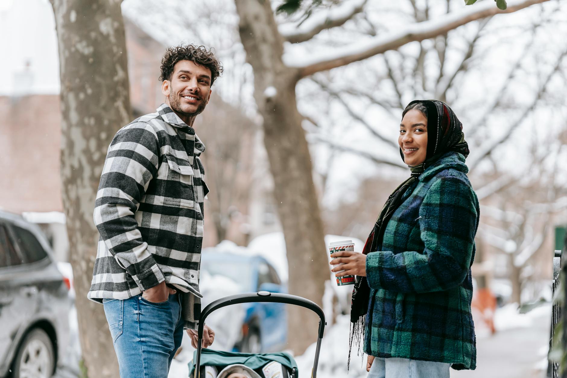 Smiling parents enjoying a winter walk with their baby in a stroller through an urban setting.