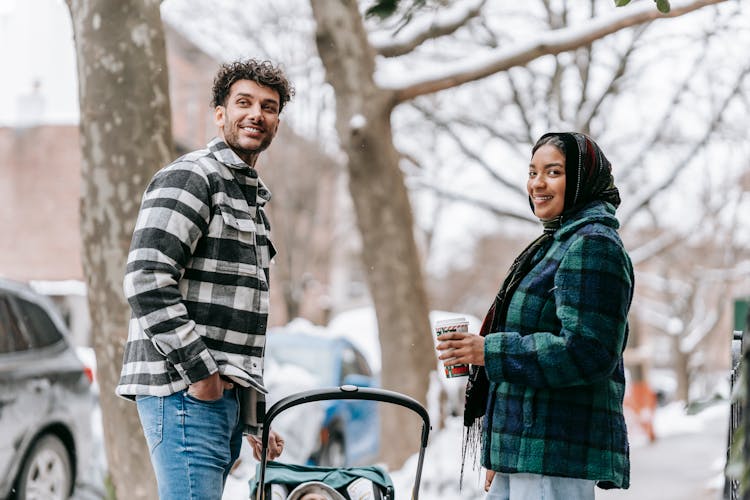 Smiling Ethnic Couple Standing On Roadside With Baby In Stroller