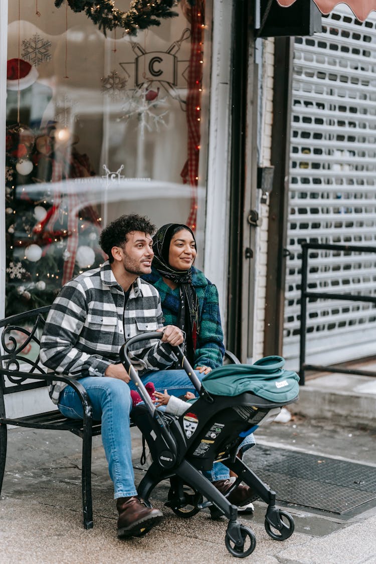 Ethnic Couple Sitting With Baby In Stroller At Christmas Holidays