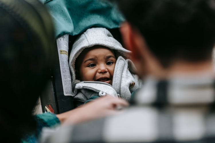 Adorable Black Toddler Boy Sitting In Stroller During Weekend With Anonymous Parents