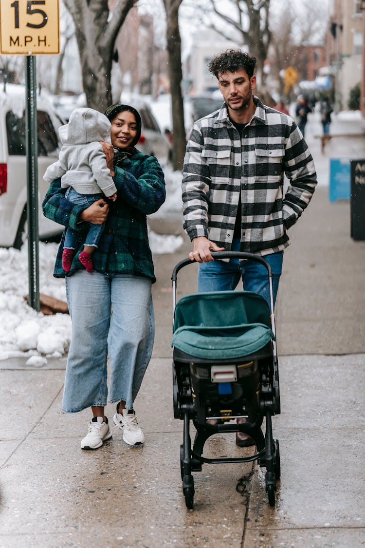 Positive Young Multiracial Couple With Baby Walking On Street