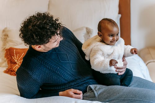 Positive diverse baby with dad having fun on bed