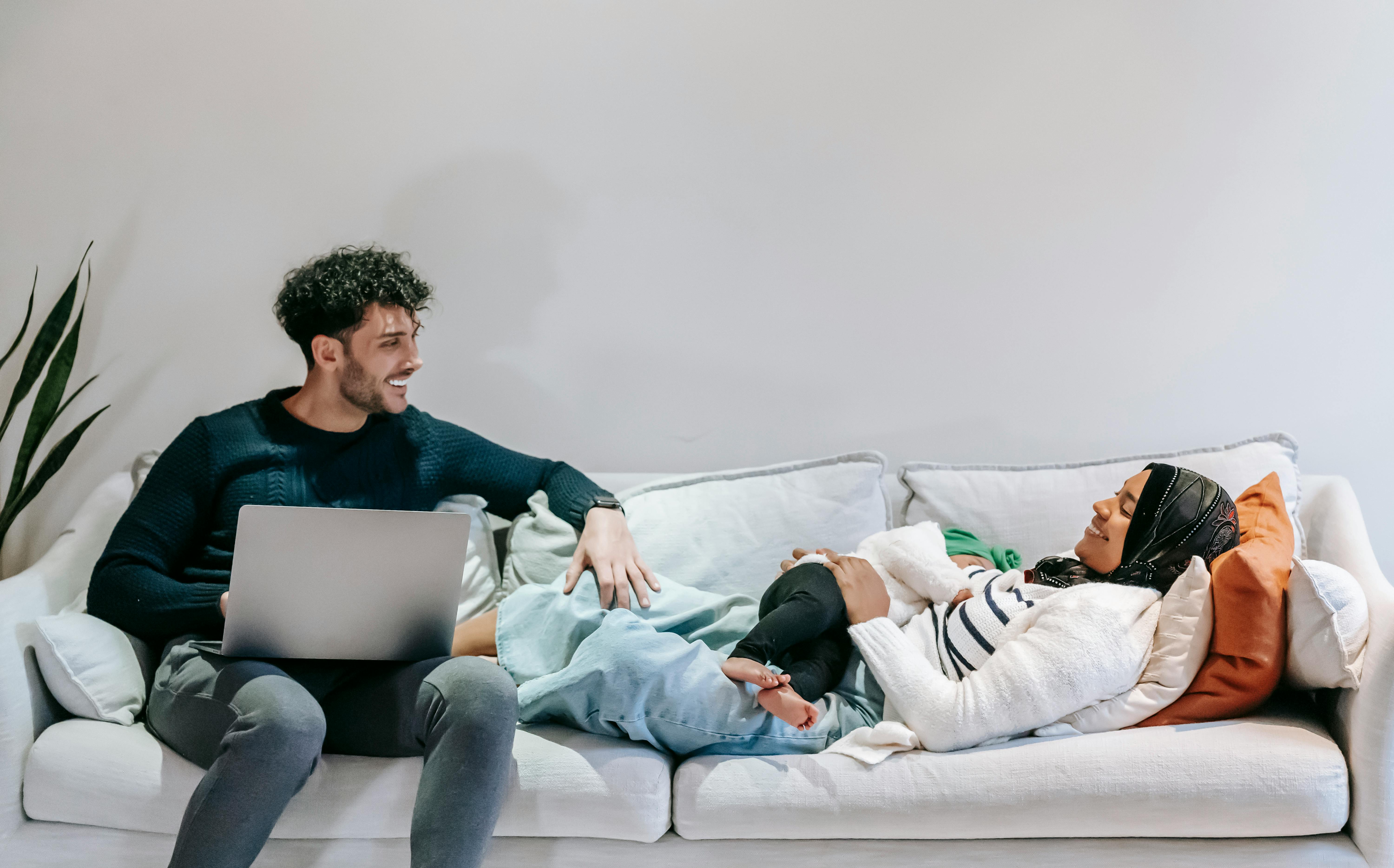 happy ethnic man using laptop while sitting near relaxing black wife and baby