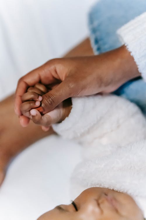 Free Anonymous ethnic woman touching hand of sleeping baby on bed Stock Photo